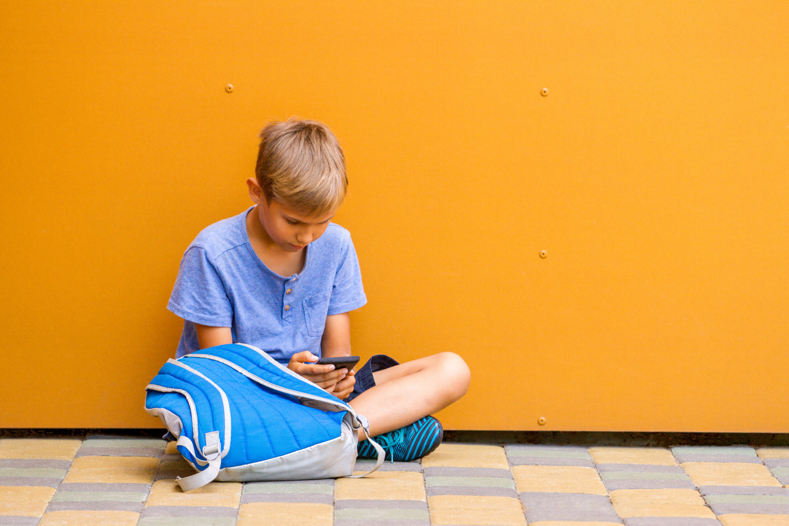 Boy with smartphone sitting on the ground symboolising social media usage among kids under 16