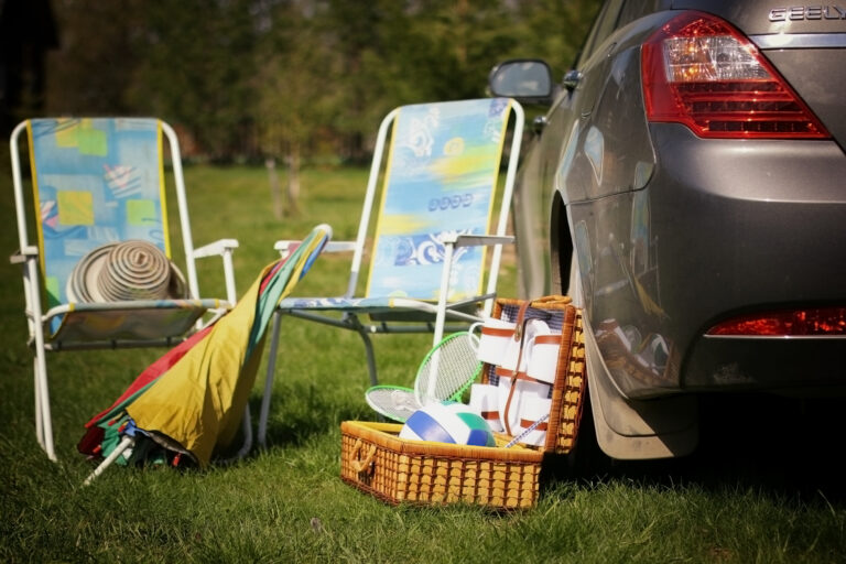 Picnic chairs, basket and plates around a parked car to symbolise local travel , picnic